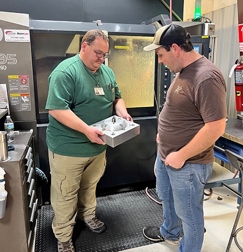 Two machinists examining a custom machined part in a CNC shop, showcasing hands-on collaboration and the use of advanced machining technology.