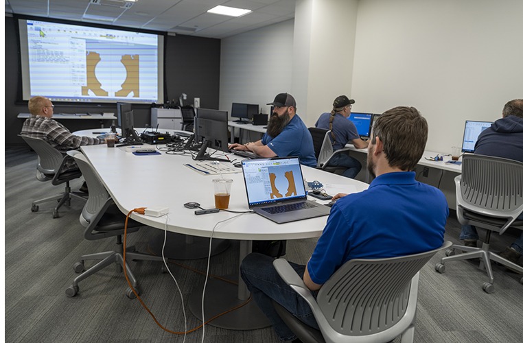 Training session in Ariel Technologies' classroom, featuring participants engaging with Mastercam CAD/CAM software on computers, projection screen displaying design graphics, modern classroom setting with collaborative layout.