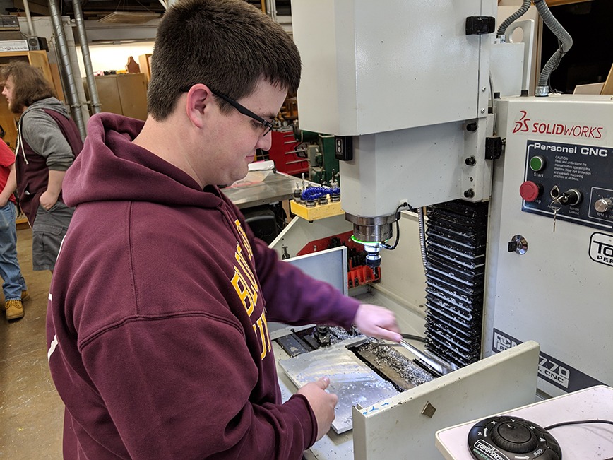 Student operating CNC machine in technology education lab, demonstrating CAD/CAM skills relevant to robotics and manufacturing programs.