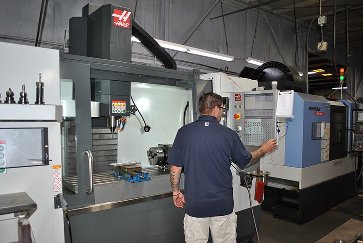 CNC supervisor operating a Haas VF-4 vertical mill, utilizing Mastercam Dynamic toolpaths for machining, with a Doosan machine visible in the background.