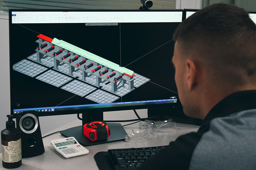 CNC Programmer reviewing a modular fixturing setup on a computer screen using Mastercam software, with tools and materials on the desk.
