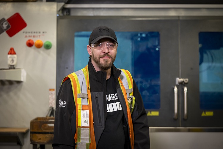 Jay Hale in safety gear standing in front of an additive manufacturing machine, showcasing Nicholson Manufacturing's advanced manufacturing processes for debarker knives.