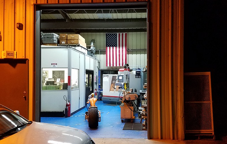 Machine shop entrance featuring a CNC machining center, manual tools, and an American flag, highlighting advanced machining capabilities for telescope instrument production.