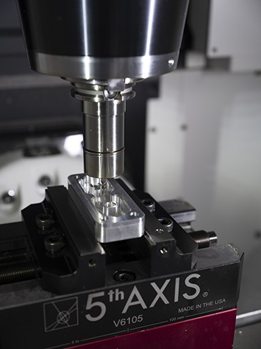 CNC machining process on a 5th Axis V6105 mill, featuring a precision test piece being machined from 6061 aluminum, showcasing Mastercam software application in a training environment.