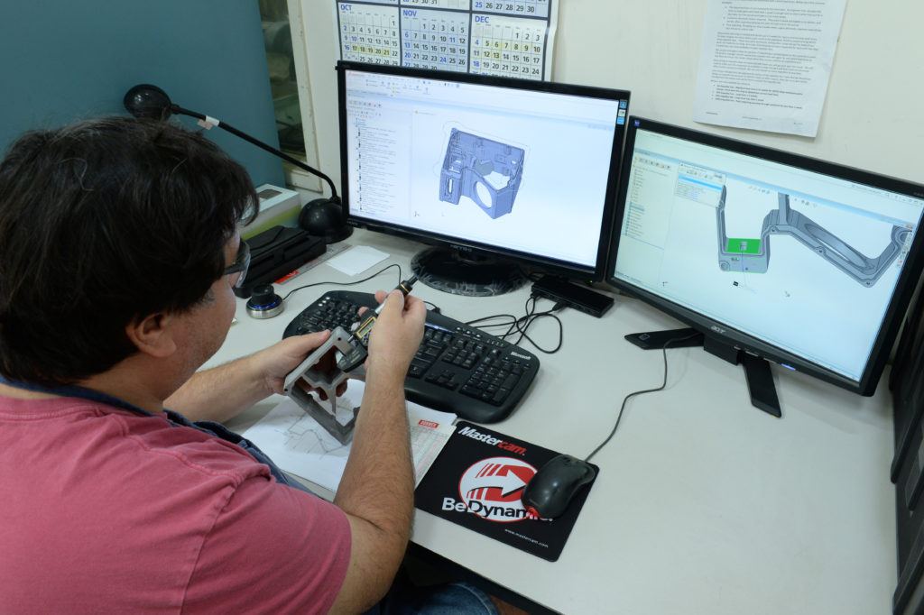 Engineer working with prototype part and Mastercam CAD/CAM software on dual monitors, showcasing design and machining integration for precise engineering solutions.
