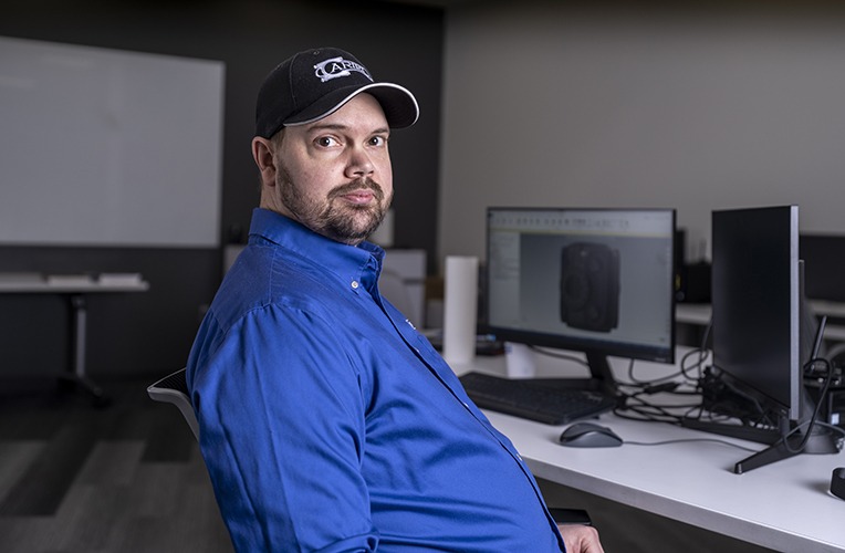 Phil Ott, Staff Group Leader of Technical Training at Ariel Technologies, seated at a workstation with Mastercam software on display, in a modern CNC Programming Lab setting.
