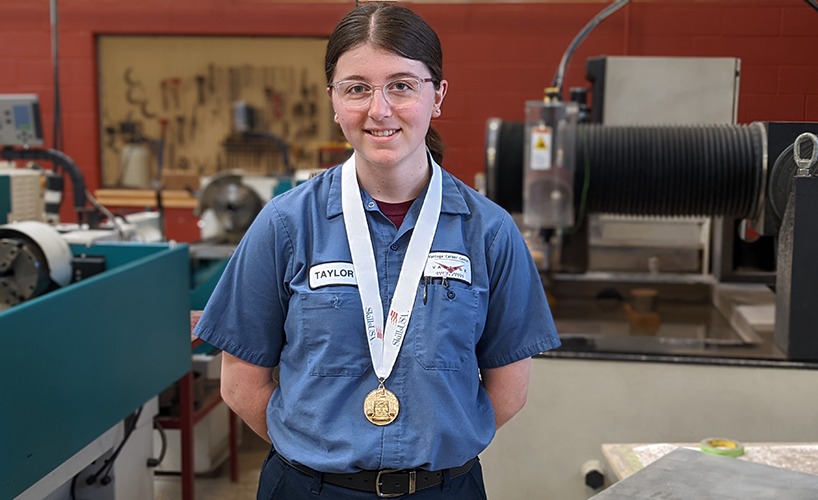 Taylor Lucas, wearing a SkillsUSA medal, stands proudly in a precision machining workshop at Vantage Career Center, showcasing the hands-on education and achievements of students in the program.