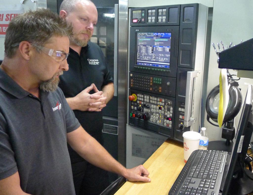 Two technicians analyzing CNC machine programming on a control panel, demonstrating advanced manufacturing techniques and Mastercam software use in Carolina Precision Components' operations.