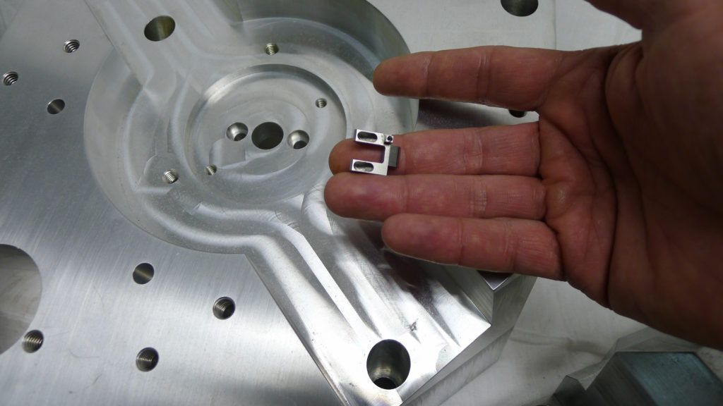 Hand holding a small precision machined part above a larger aluminum component, illustrating advanced CNC machining processes used by Carolina Precision Components.