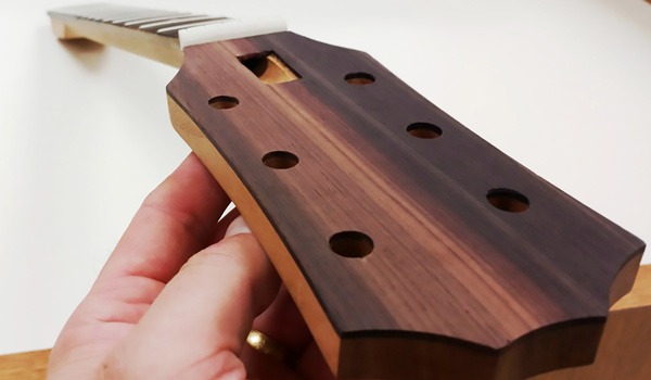 Guitar neck with fret slots and tuning peg holes, held by a hand, showcasing craftsmanship in guitar making at Reed-Custer High School's Industrial Technology program.