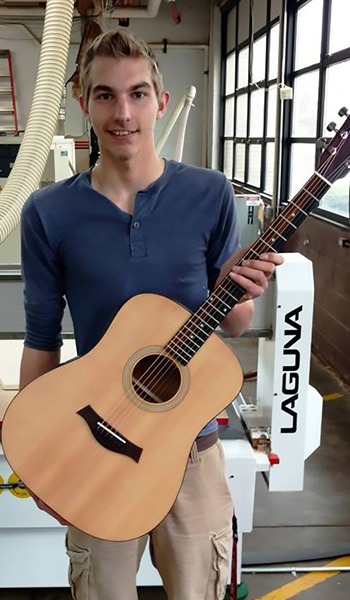 Student at Reed-Custer High School holding a handcrafted guitar in a woodworking lab, showcasing the practical application of advanced manufacturing techniques and woodworking education.