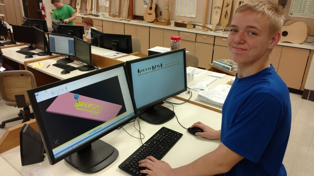Student using Mastercam software to design a woodworking project on dual monitors in Reed-Custer High School's Industrial Technology classroom, showcasing CAD/CAM technology in action.
