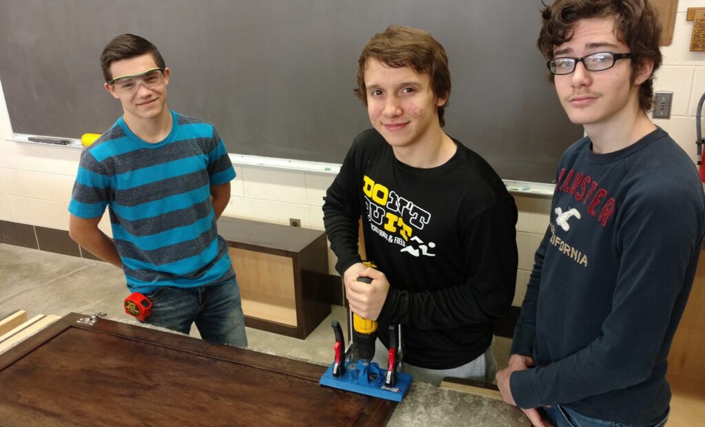 Students in Reed-Custer High School's Industrial Technology program working on woodworking projects, using tools and equipment for cabinet assembly, with a focus on hands-on learning and advanced manufacturing techniques.