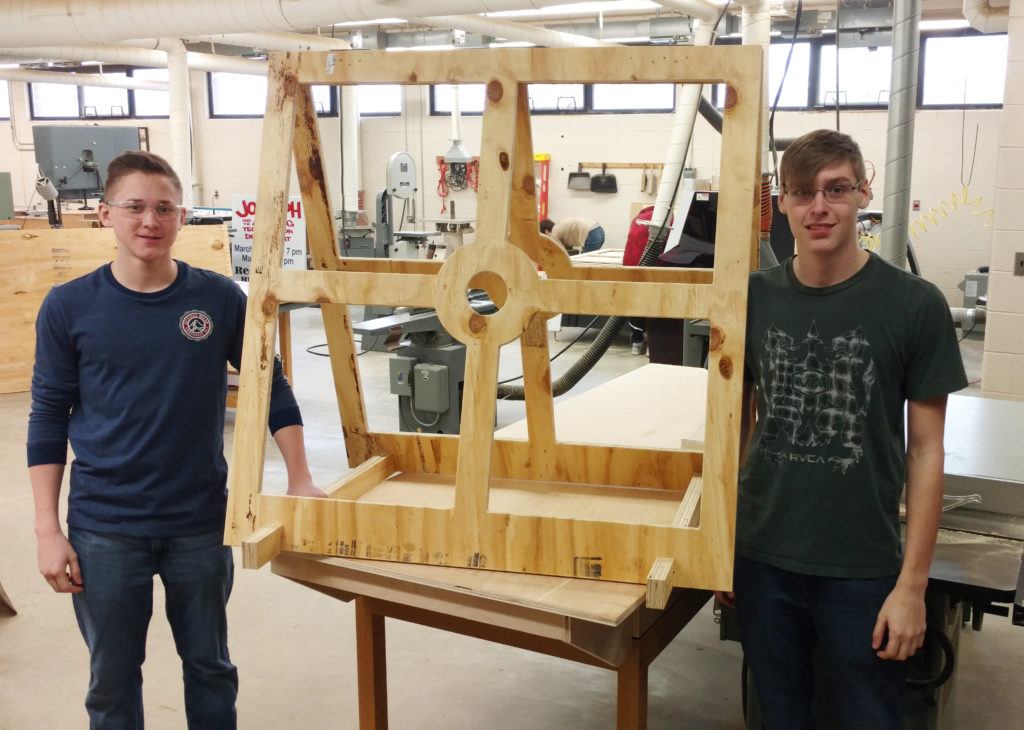 Students at Reed-Custer High School's Industrial Technology program showcasing a wooden project frame in a woodworking shop, emphasizing hands-on learning and advanced manufacturing techniques.