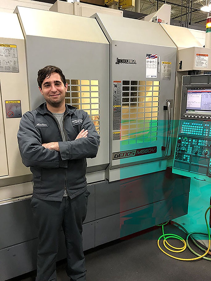 CNC programmer standing confidently beside an Okuma GENOS M560V machining center, showcasing advanced manufacturing capabilities at United Machine & Metal Fabrication.
